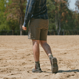 Man walking on land wearing the Soft Toe Rainier Boots Olive Green, shorts, and a long-sleeve shirt in an outdoor setting.