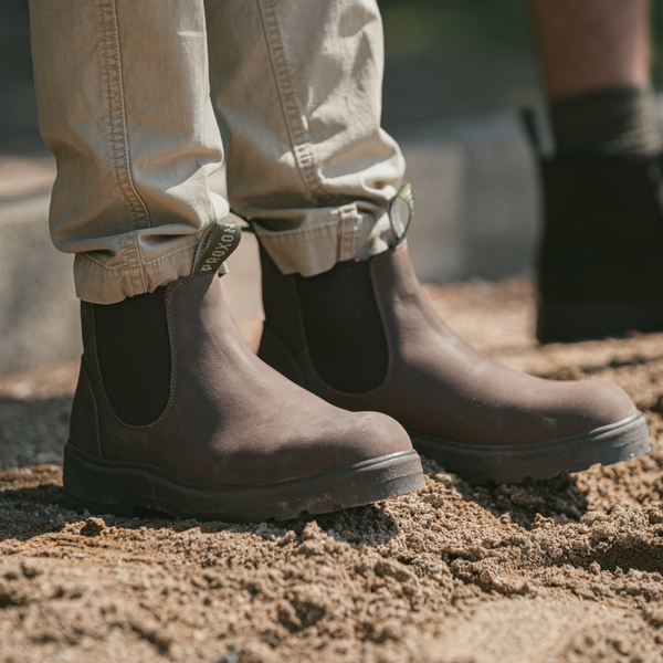 Close shot of a man wearing the Soft Toe Rainier Boots Tobacco, pants at an outdoor setting.